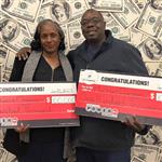 Michael and Rebecca Chesson stand in front of a money backdrop, while holding large, red Powerball checks.